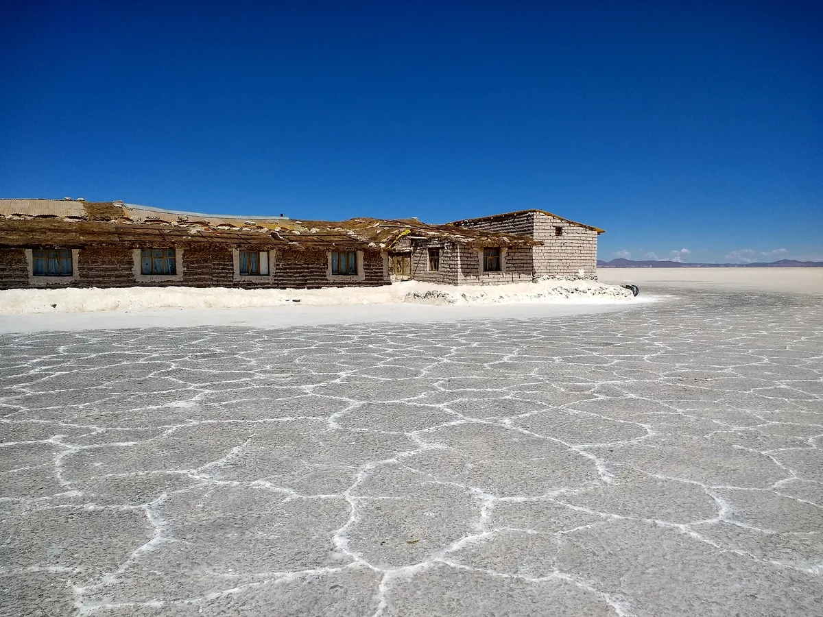 Um hotel de blocos de sal à beira da crosta branca do salar, sob um céu azul.