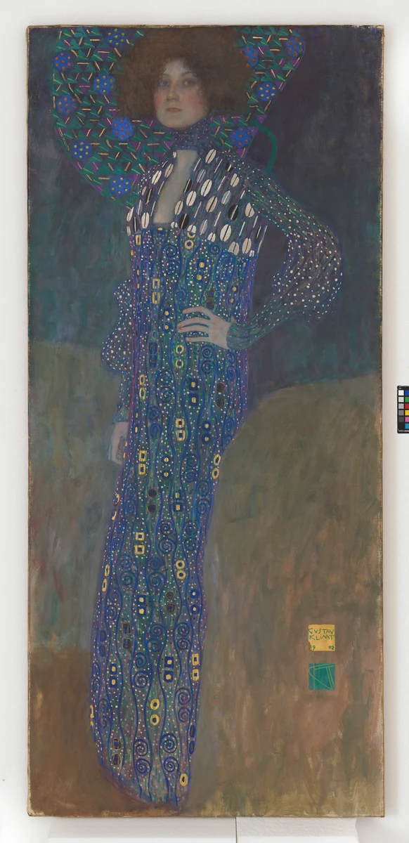 Painting of Emilie Flöge standing with one hand on her hip, wearing a long blue dress with ornamental patterns.