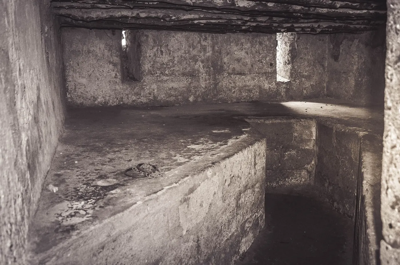 Uma sala de pedra vazia, com uma plataforma baixa e uma corrente sobre ela.